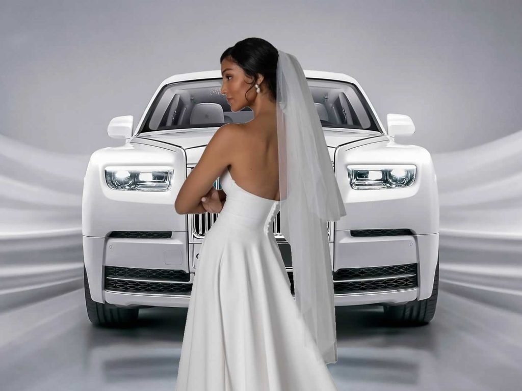 Rear view of a modern bride wearing an A-line bridal gown and short veil standing in fron of aRolls-Royce Phantom 8 Eight wedding car.