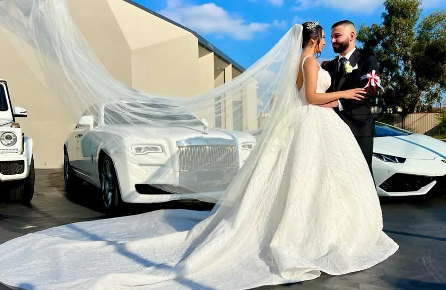 Bride and Groom standing in front of a Rolls-Royce Ghost wedding car. The bride is wearing a voluminous ball gown style wedding dress.