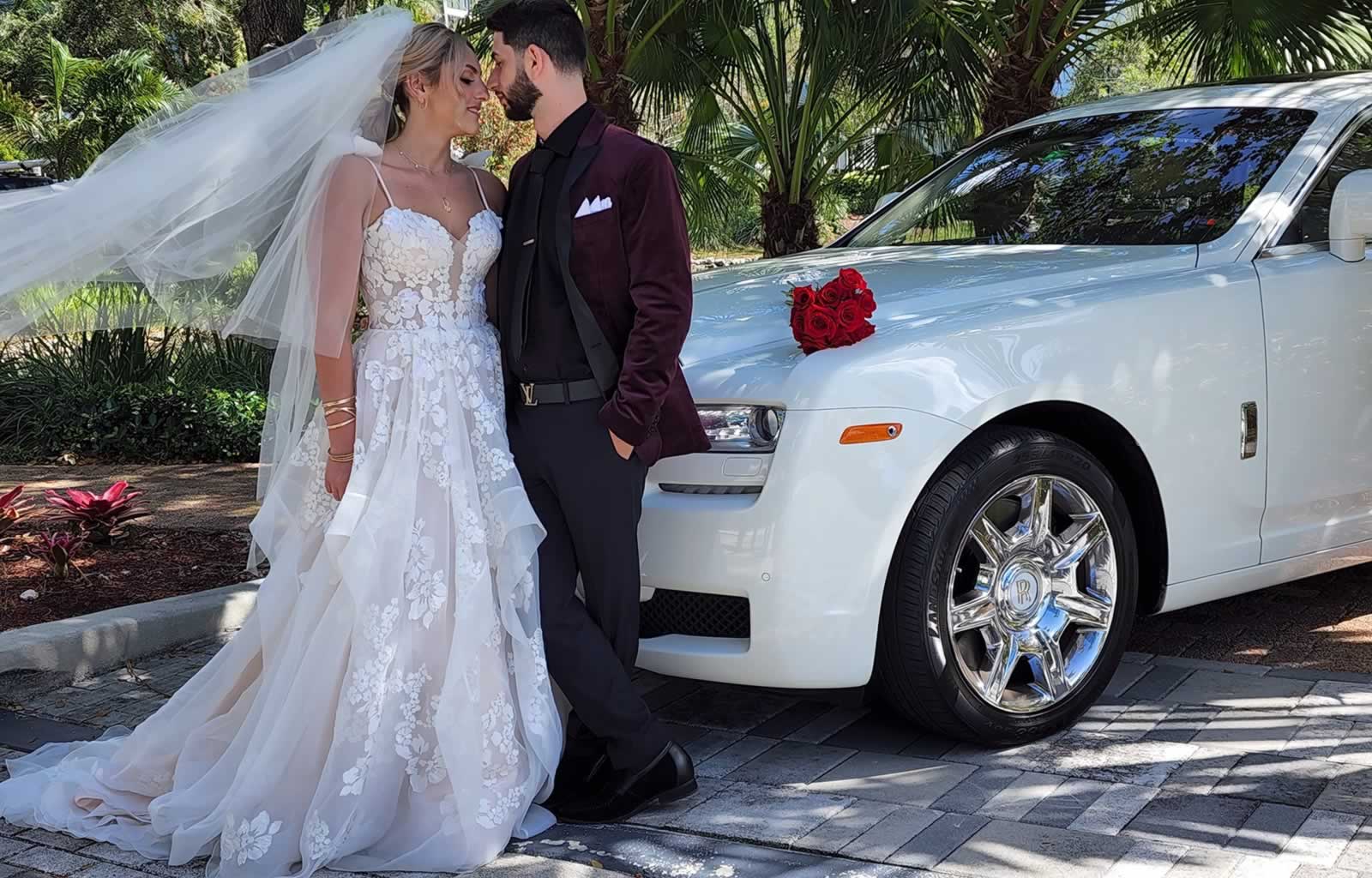 Bride (in lace bridal gown) and groom with Rolls Royce wedding car
