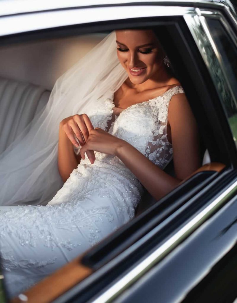 Beautiful young bride wearing an all ove slim silhouette wedding dress, seated in a Rolls-Royce wedding car.
